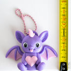 Purple bat keychain next to measuring tape for scale
