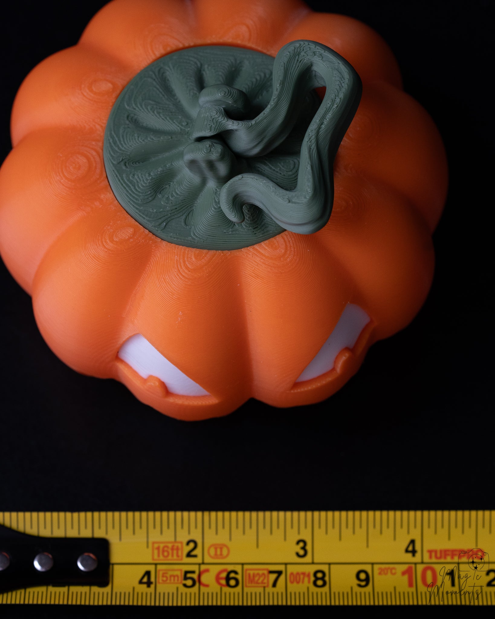Pumpkin-shaped object with a green top on a black background, measured by a yellow ruler at the bottom.