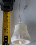 white ribbed christmas bell ornament next to measuring tape for scale