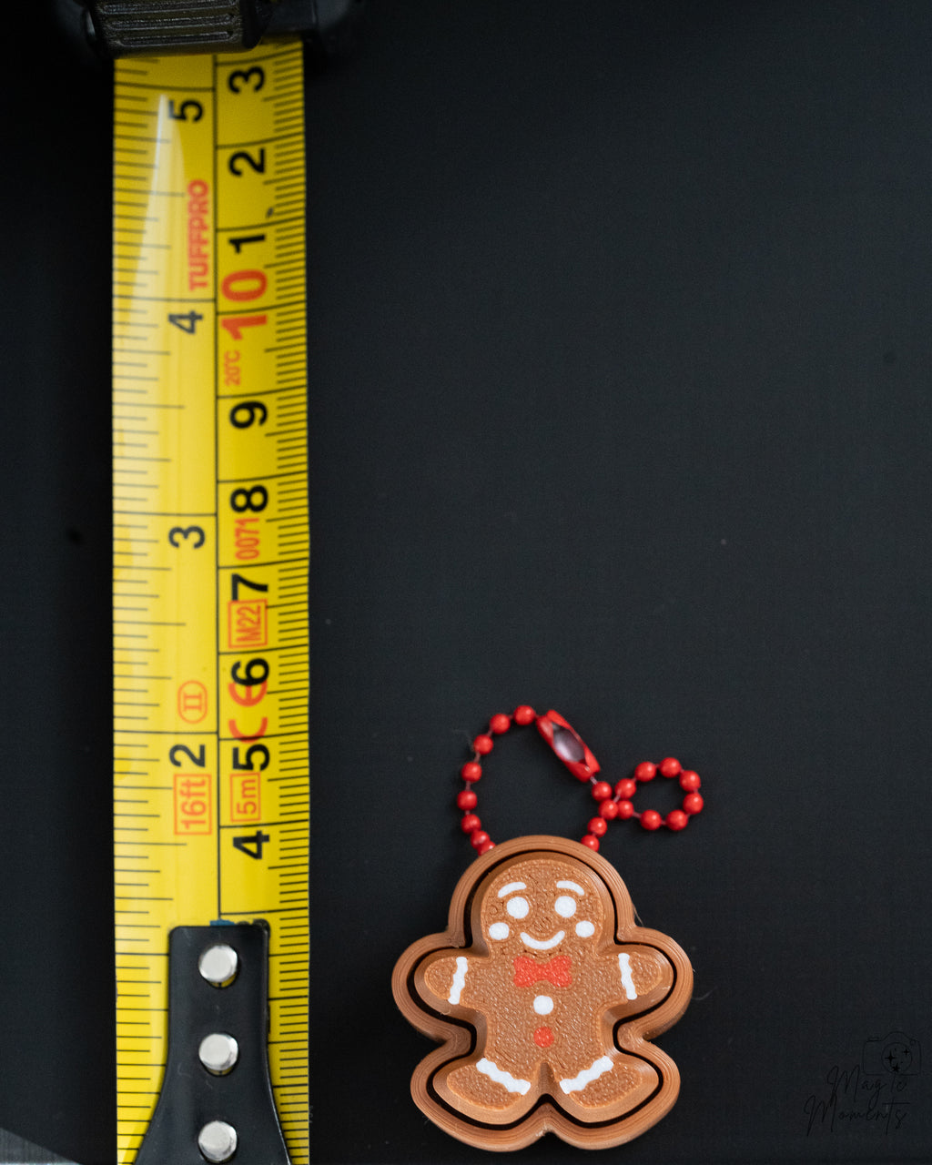 Mini gingerbread clicker with hanging loop next to measuring tape for scale