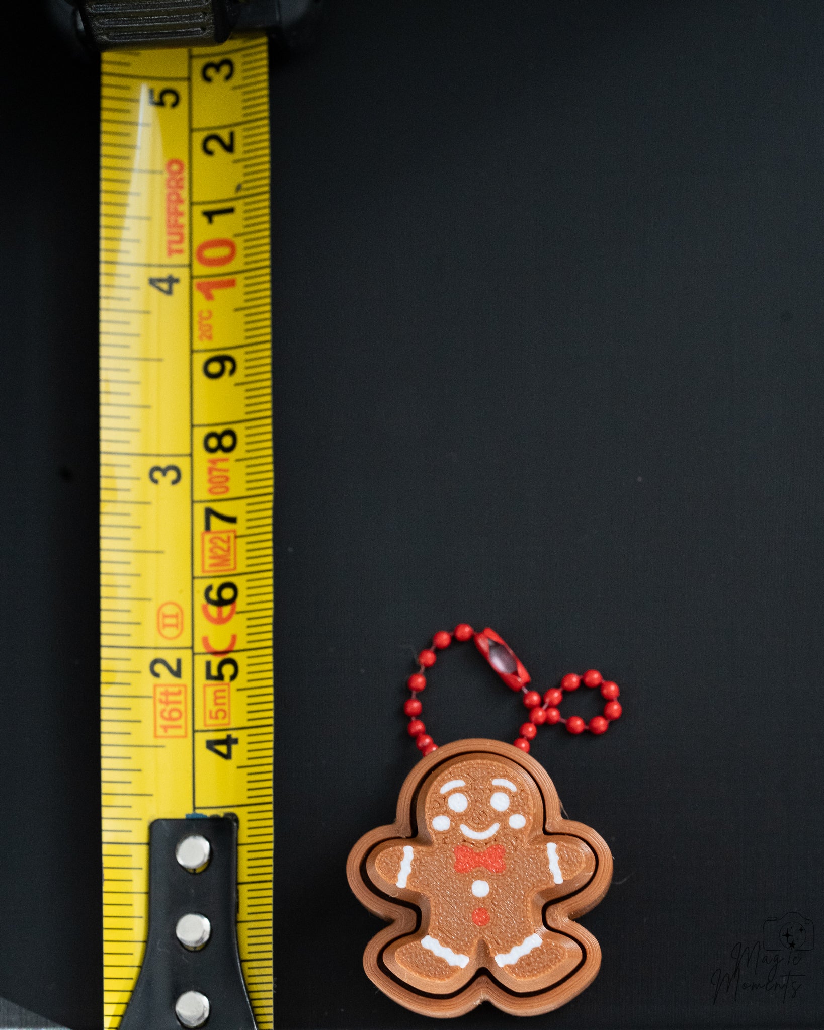 Mini gingerbread clicker with hanging loop next to measuring tape for scale