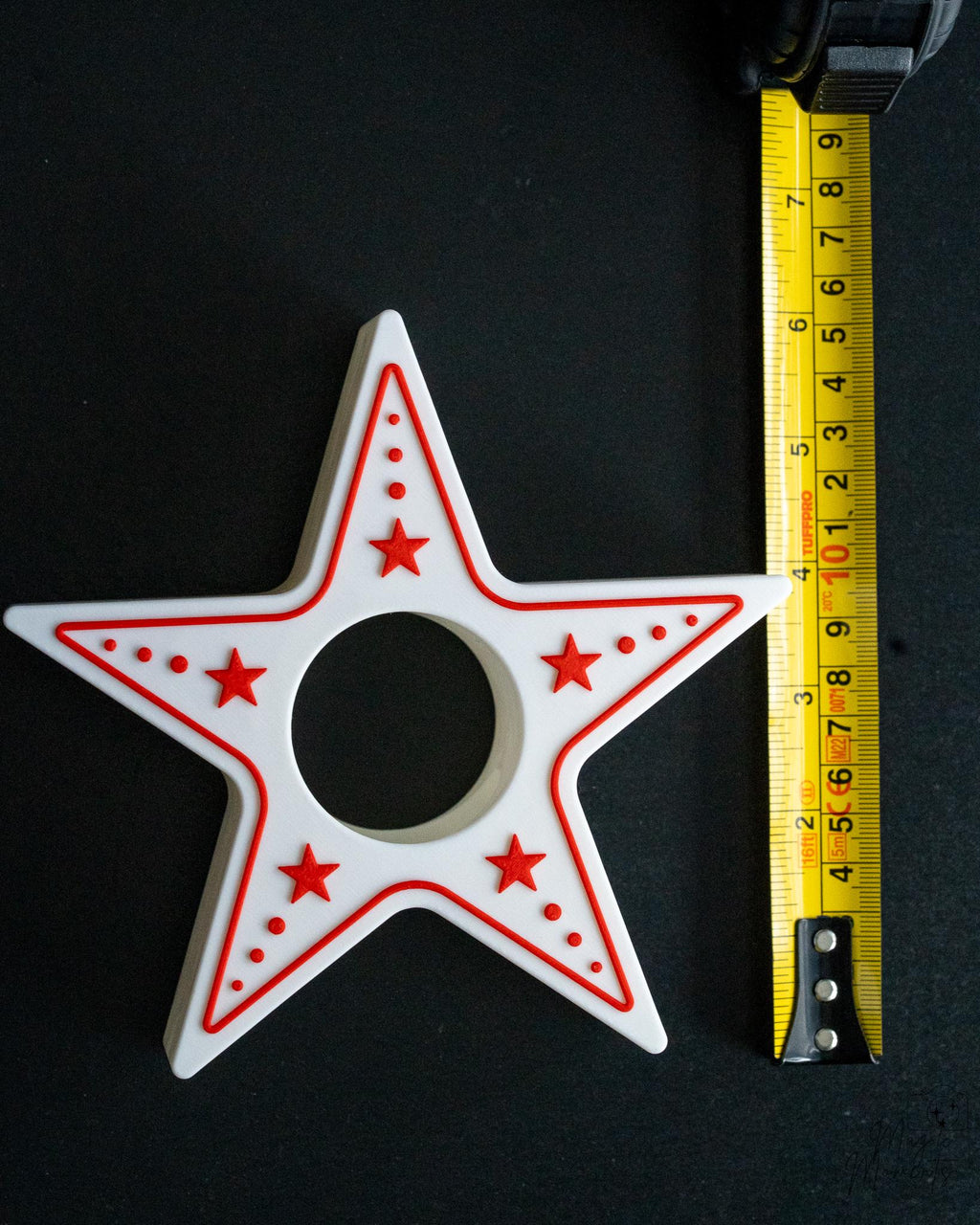 Star-shaped tealight holder with red accents on a black background, measured by a tape measure.
