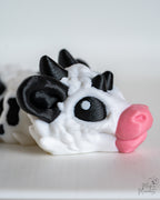 Close-up of a cow draon with black ears and pink nose on a white background