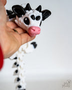 Hand holding a cow dragon with a white and black design on a light background