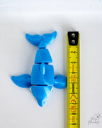 Blue articulated dolphin figure next to measuring tape for scale