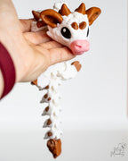 Hand holding a cow dragon with a white and brown design on a light background
