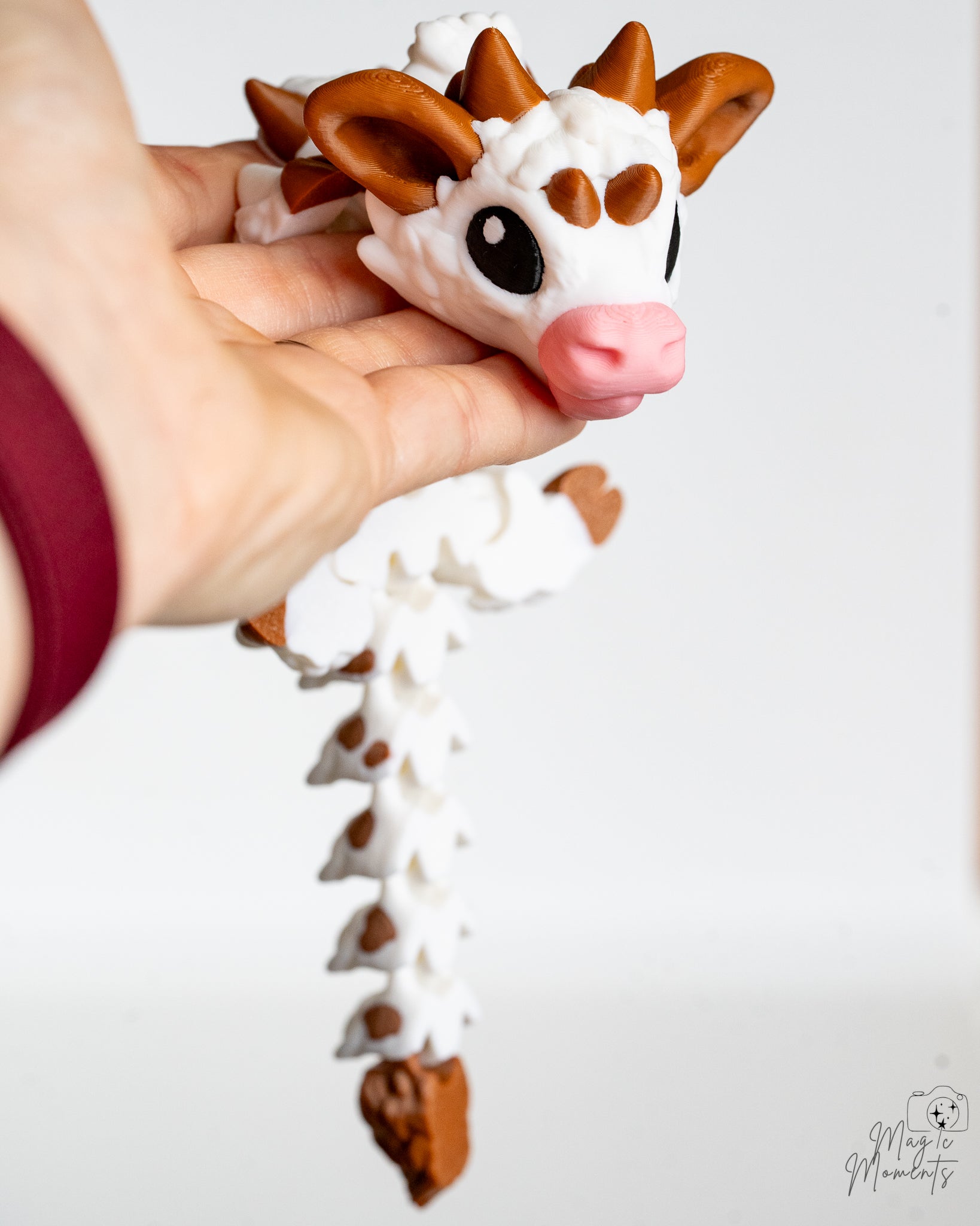 Hand holding a cow dragon with a white and brown design on a light background