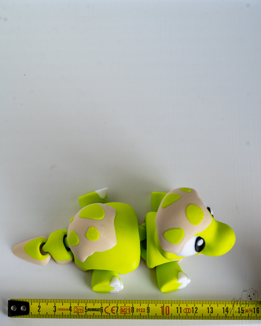 Green dinosaur figure next to measuring tape for scale