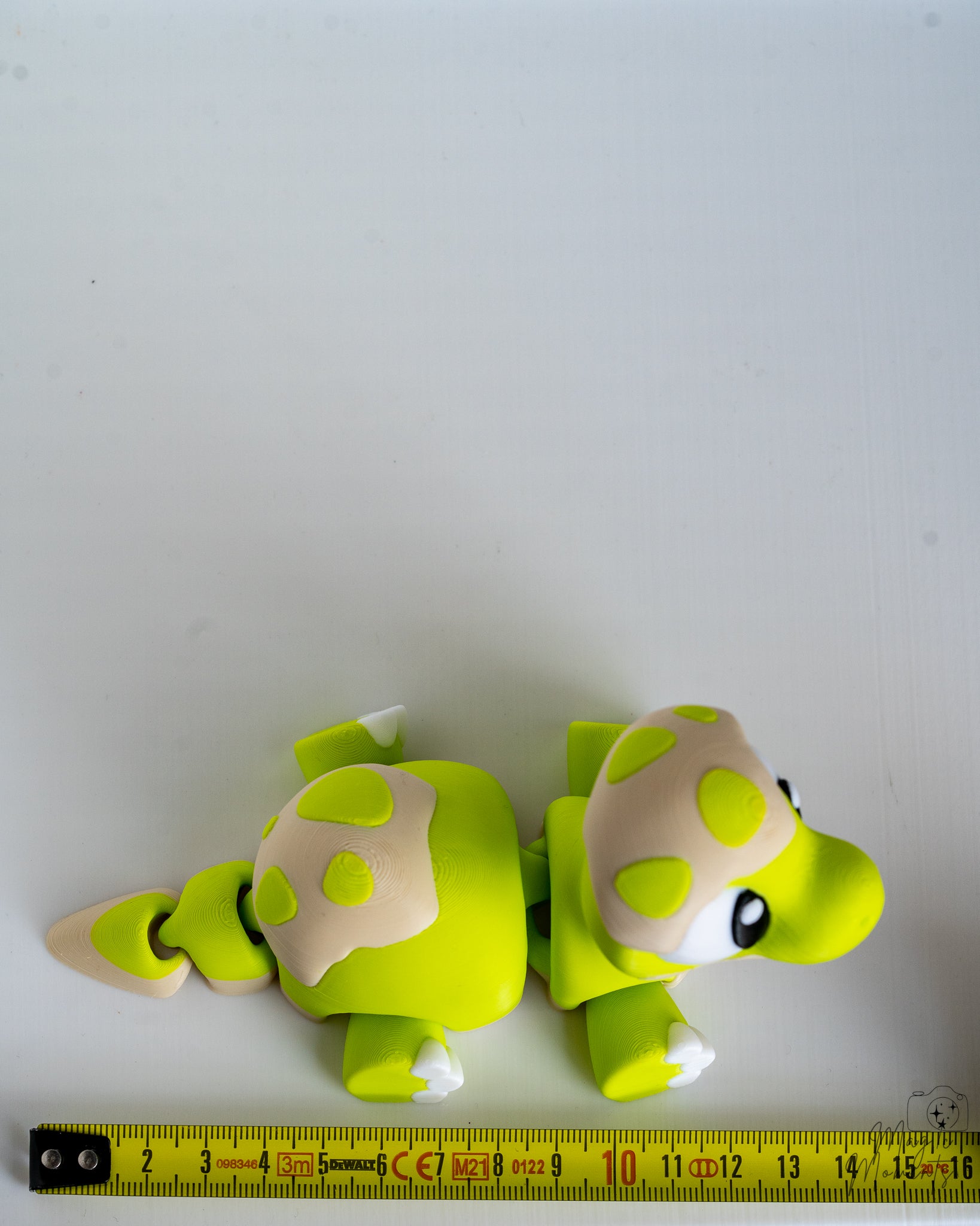 Green dinosaur figure next to measuring tape for scale
