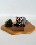 Tasmanian devil figurine with a rock and plant on a wooden base against a white background