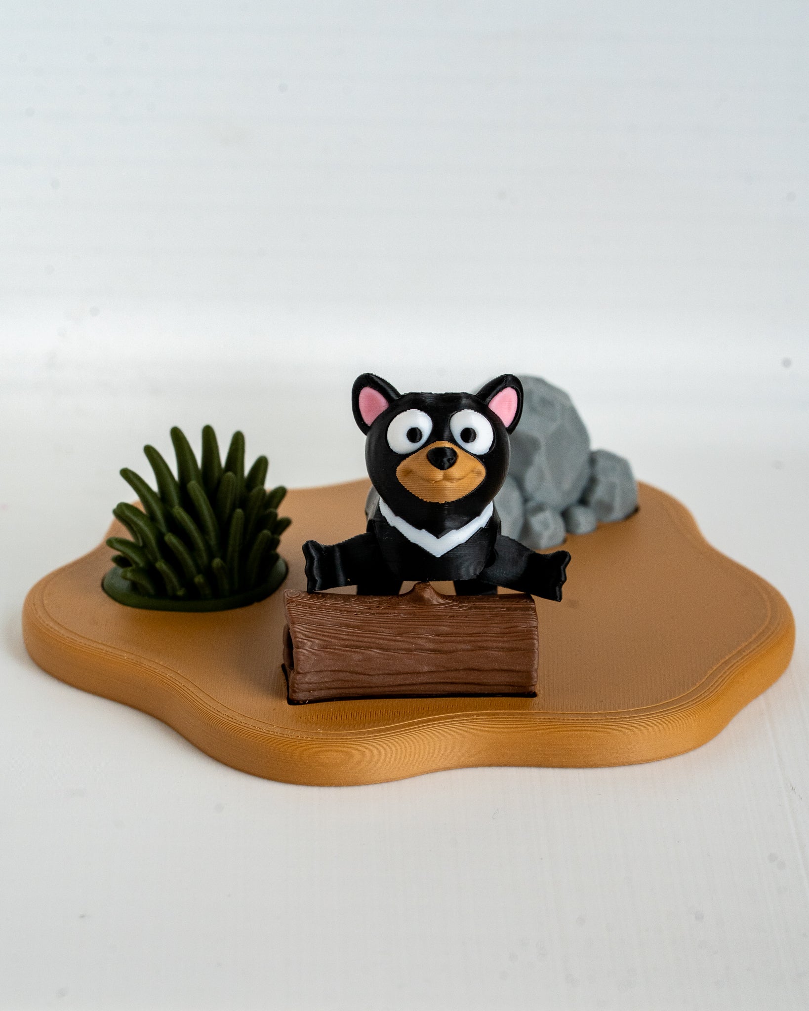 Tasmanian devil figurine with a rock and plant on a wooden base against a white background
