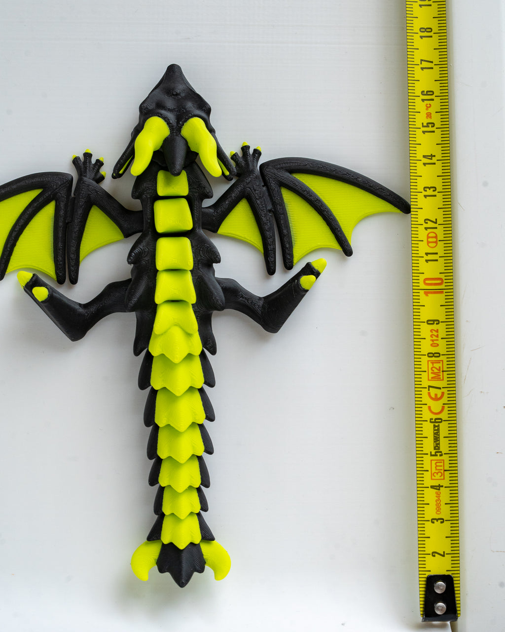 Black and green dragon next to a measuring tape on a white background