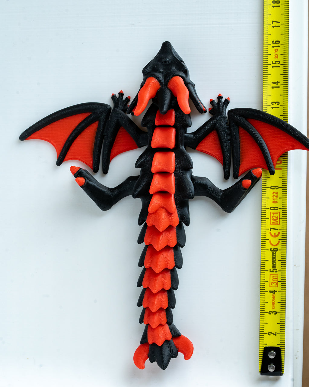 Red and black dragon with a measuring tape  for scale on a white background