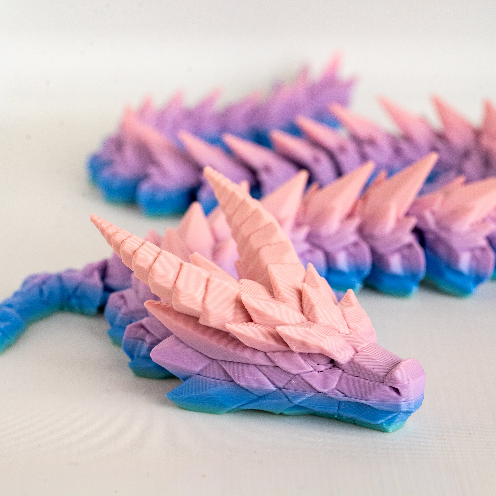 Colorful dragon with a gradient of pink, purple, and blue on a white background.
