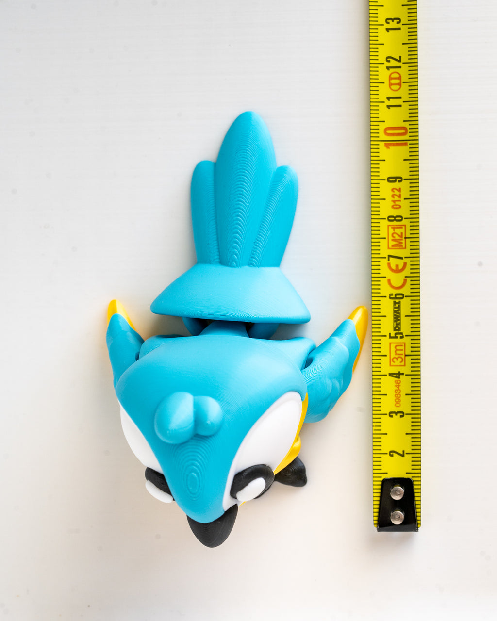 Blue parrot figurine next to a ruler on a white background