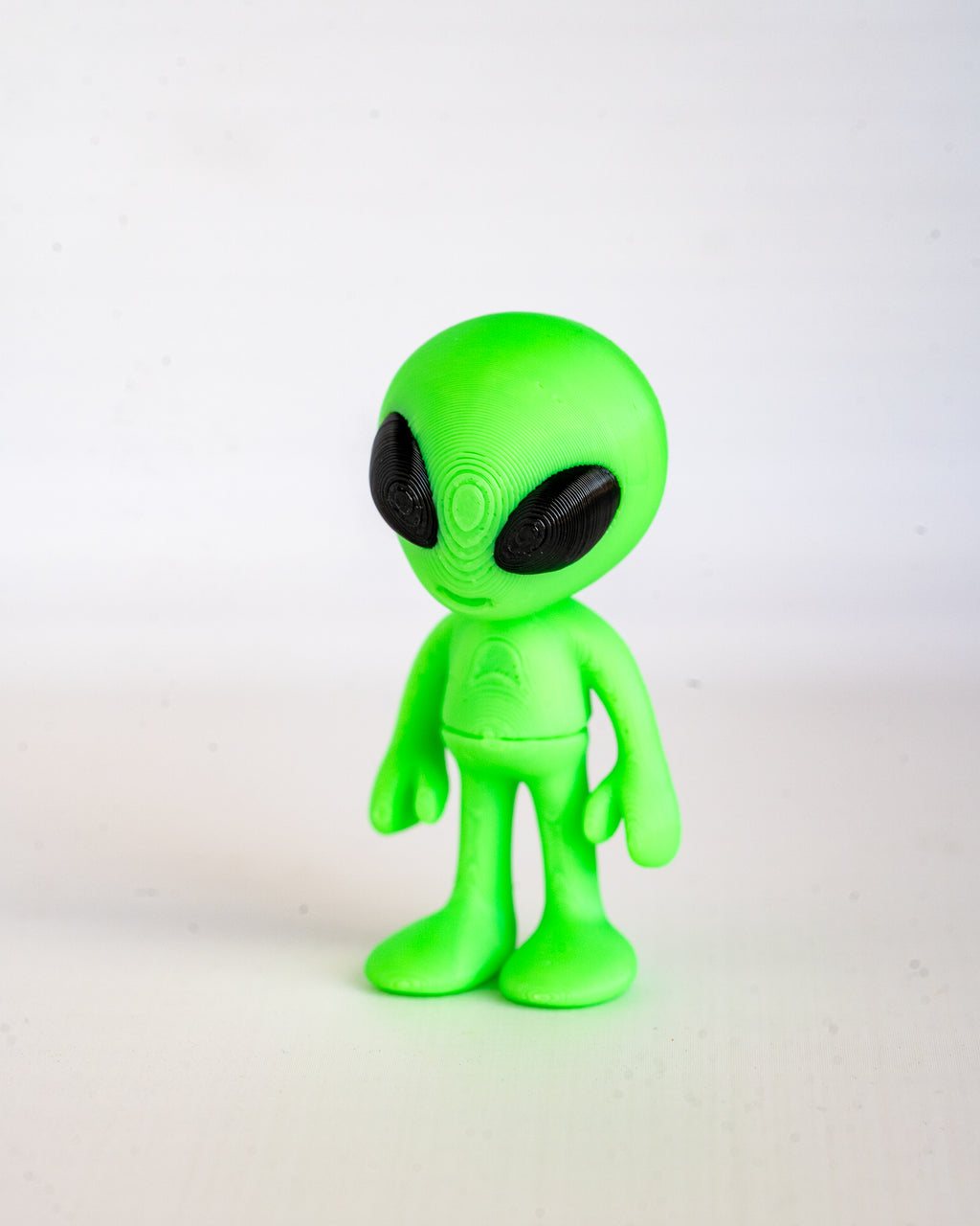 A small green alien figurine with large black eyes, standing against a plain white background.