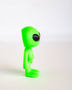 A small bright green alien figurine with a large black eye, standing in profile against a plain white background.
