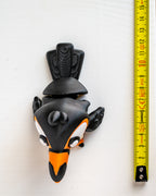 toucan figurine next to a yellow measuring tape on a white background.