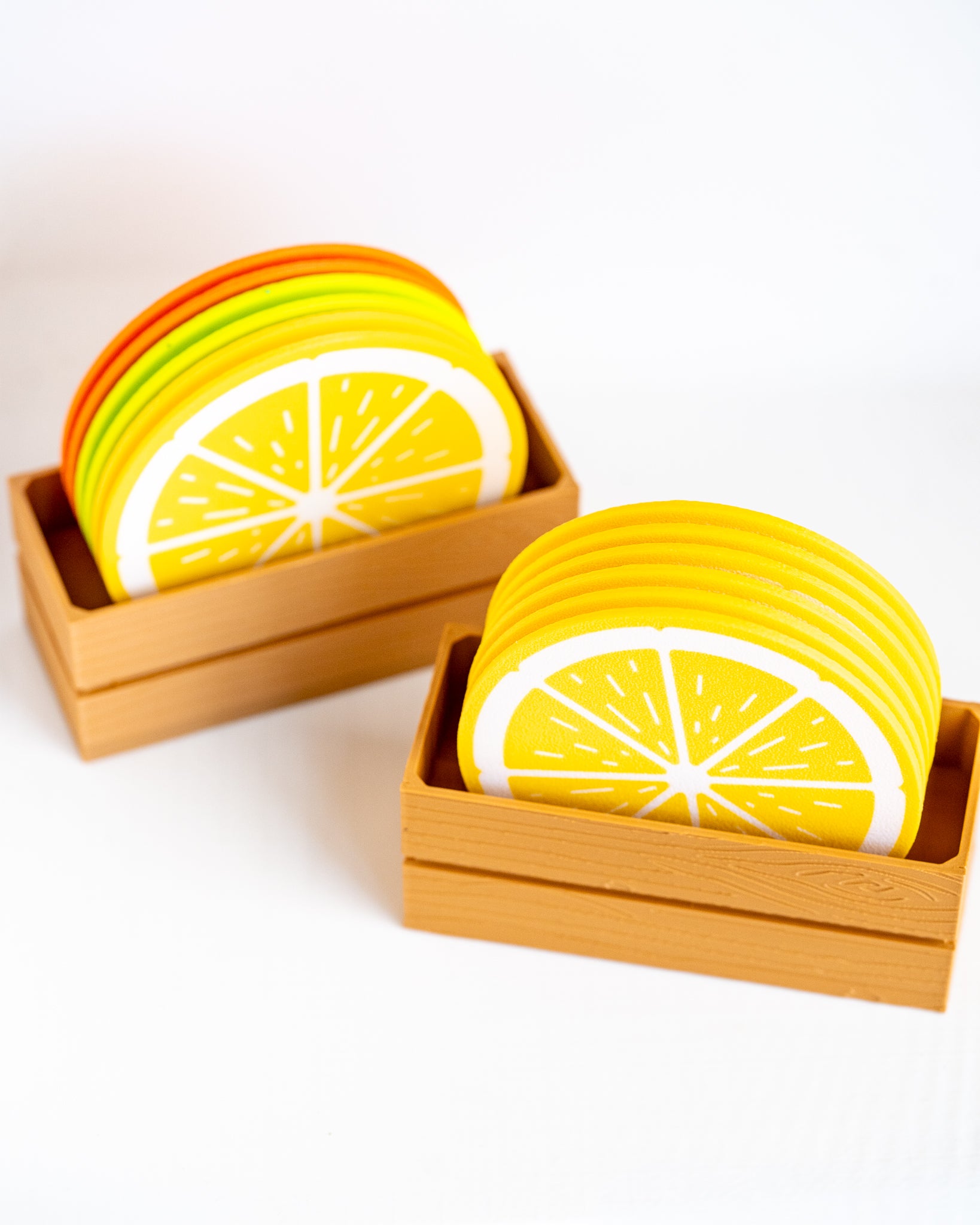 Two small wooden trays holding stacks of round coasters printed with bright yellow lemon slice designs on a clean white background.