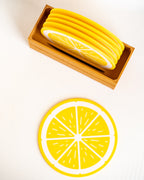 Yellow and white lemon slice coasters, including a stack of round coasters in a wooden tray and one flat coaster displayed below on a white background.