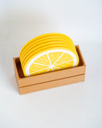 A stack of round coasters designed to look like yellow lemon slices, displayed inside a light wood tray on a clean white background.
