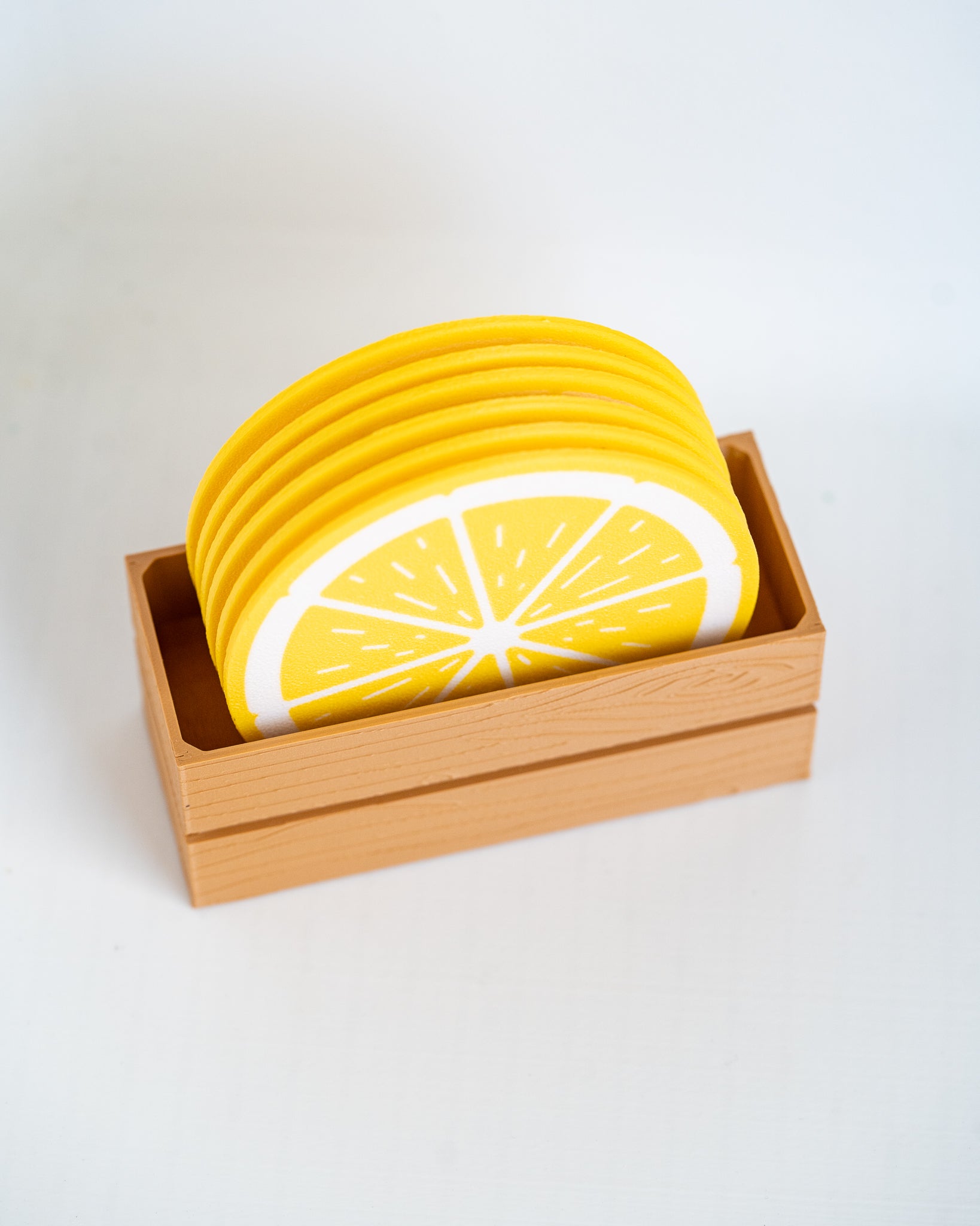 A stack of round coasters designed to look like yellow lemon slices, displayed inside a light wood tray on a clean white background.