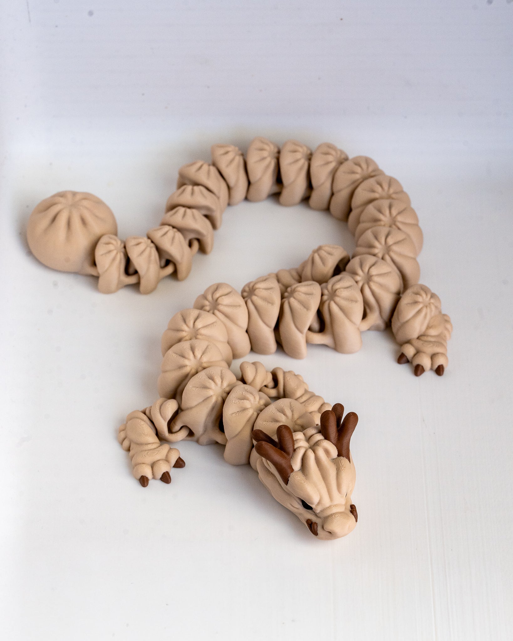 A beige dragon figurine 3d printed posed in a curved S-shape on a plain white background.