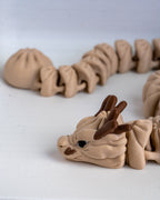 A close-up of a beige 3d printed dragon figurine with dark brown horns and ears