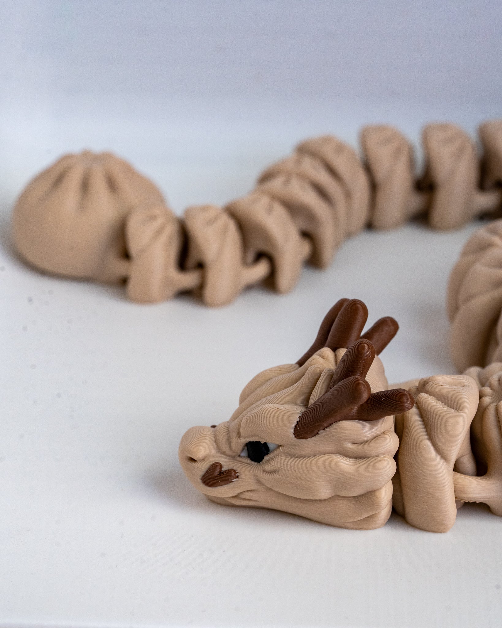 A close-up of a beige 3d printed dragon figurine with dark brown horns and ears