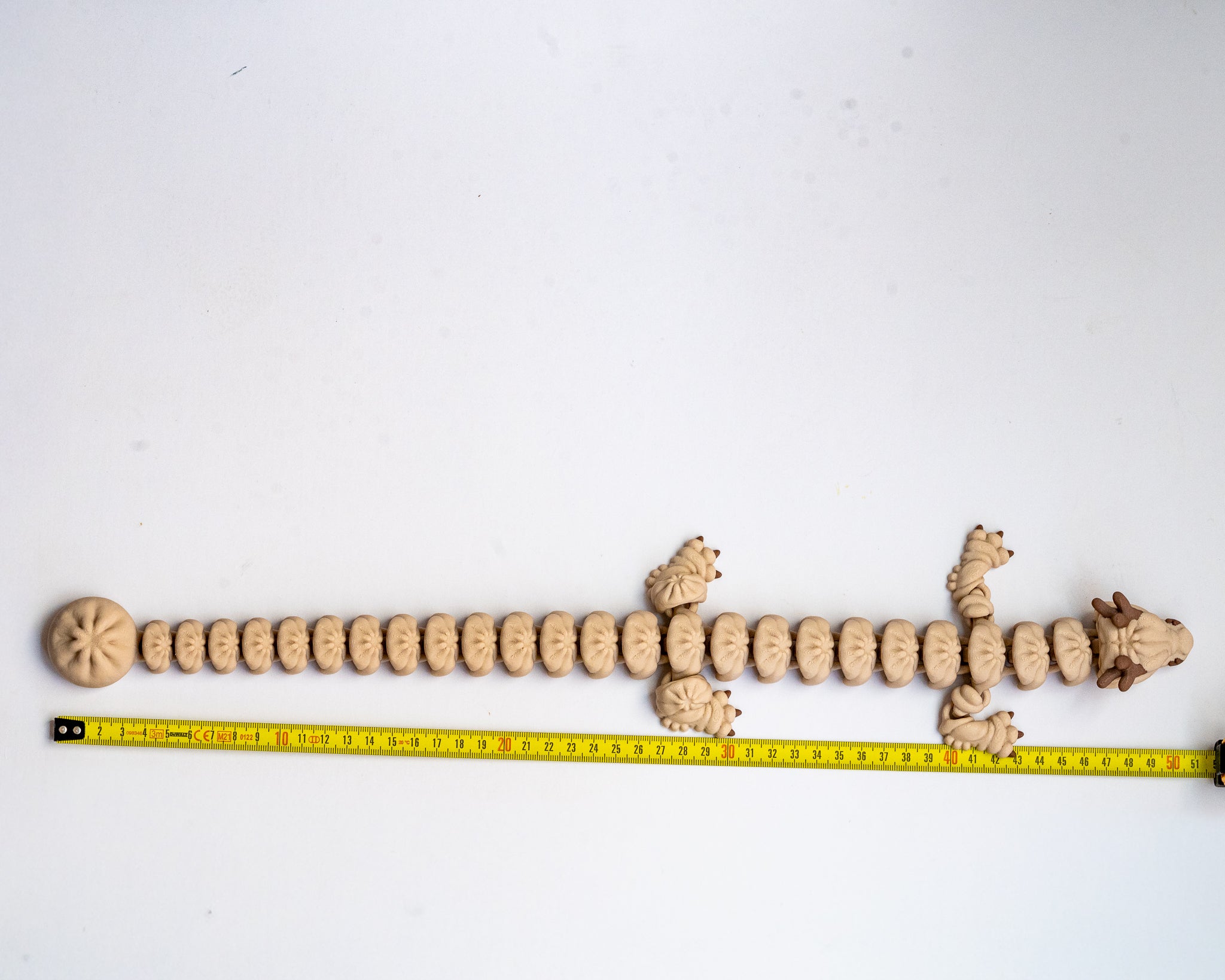 long 3d printed dumpling dragon figurine next to a measuring tape for a scale