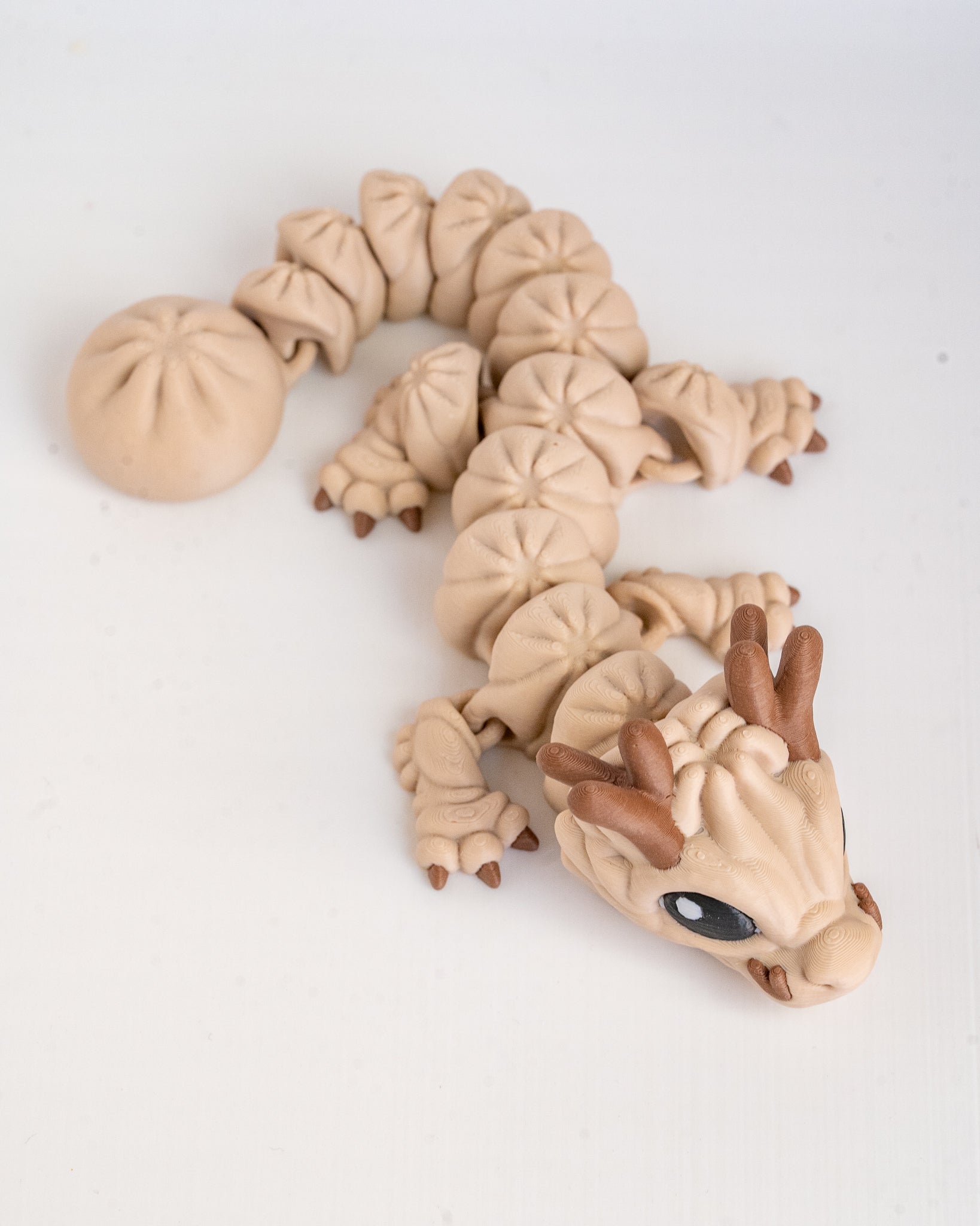 A small dragon figurine, posed on a plain white background. The dragon has a segmented body, small claws, and a snout with a glossy black eye.