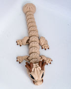 A small dragon figurine or toy made of beige and brown pla, photographed on a plain white background.