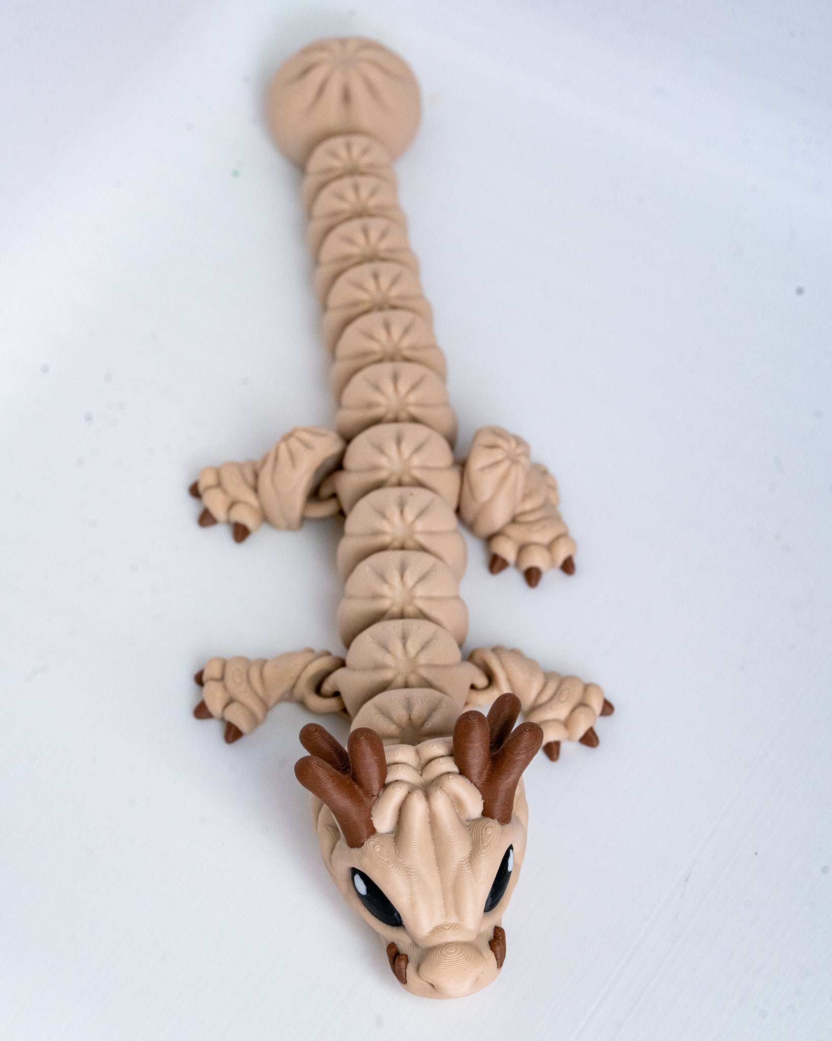 A small dragon figurine or toy made of beige and brown pla, photographed on a plain white background.
