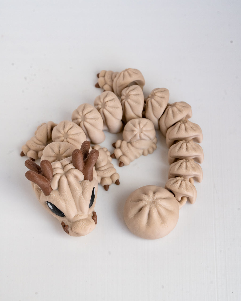 3d printed dragon figurine made of beige and brown pla on a plain white background. 