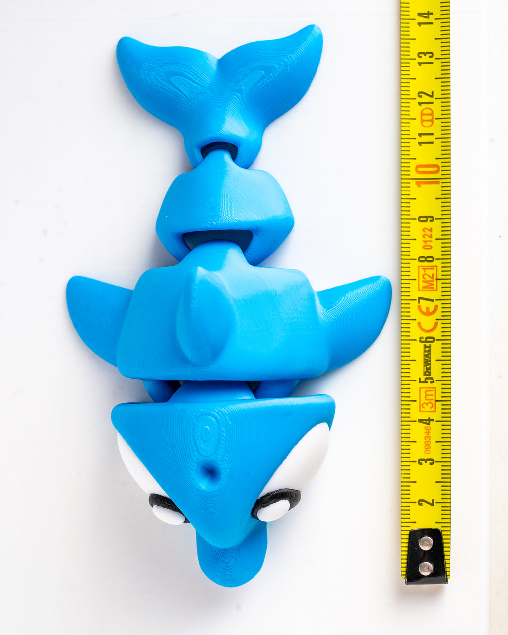 A bright blue fish-shaped product shown vertically next to a yellow measuring tape on a plain white background.