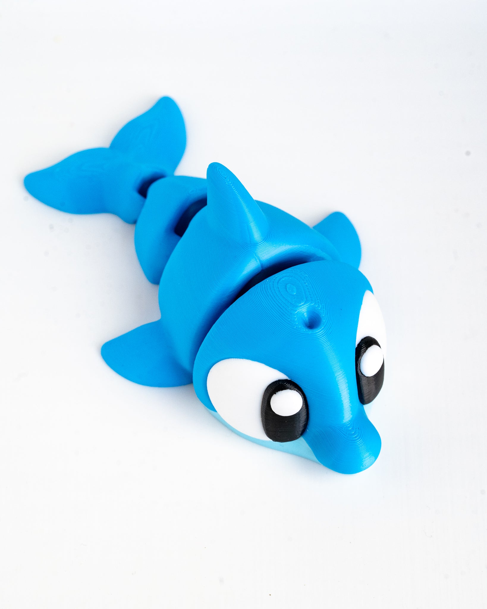 A bright blue plastic dolphin toy with large cartoon eyes, photographed on a plain white background.