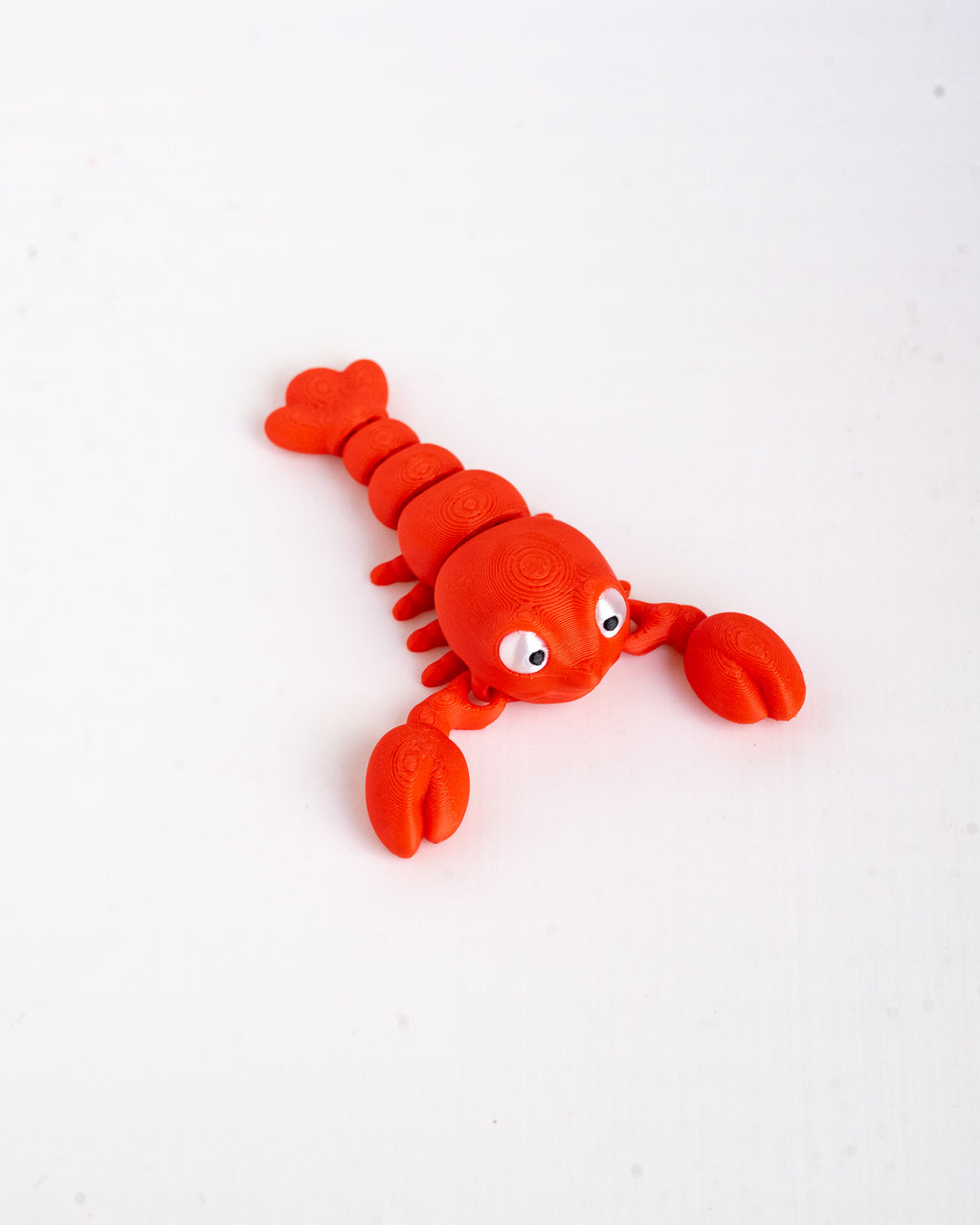 A bright red plastic toy lobster with cute white eyes, photographed on a clean white background.