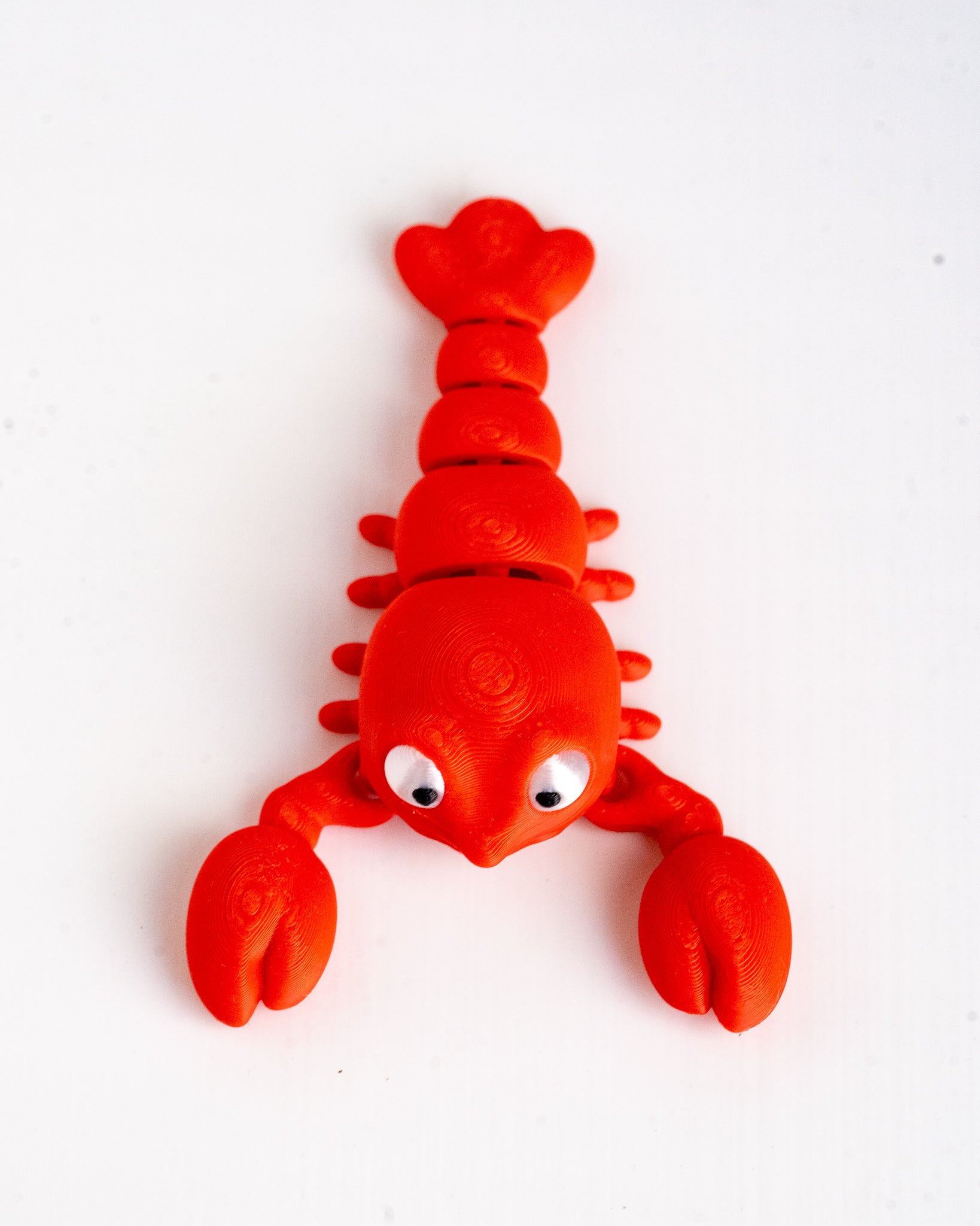 A bright red lobster-shaped toy or decoration with large white eyes, photographed on a plain white background.