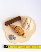 A small animal figurine of a pangolin on a beige base with a brown log, gray rocks, and beige hills, photographed on a white background.