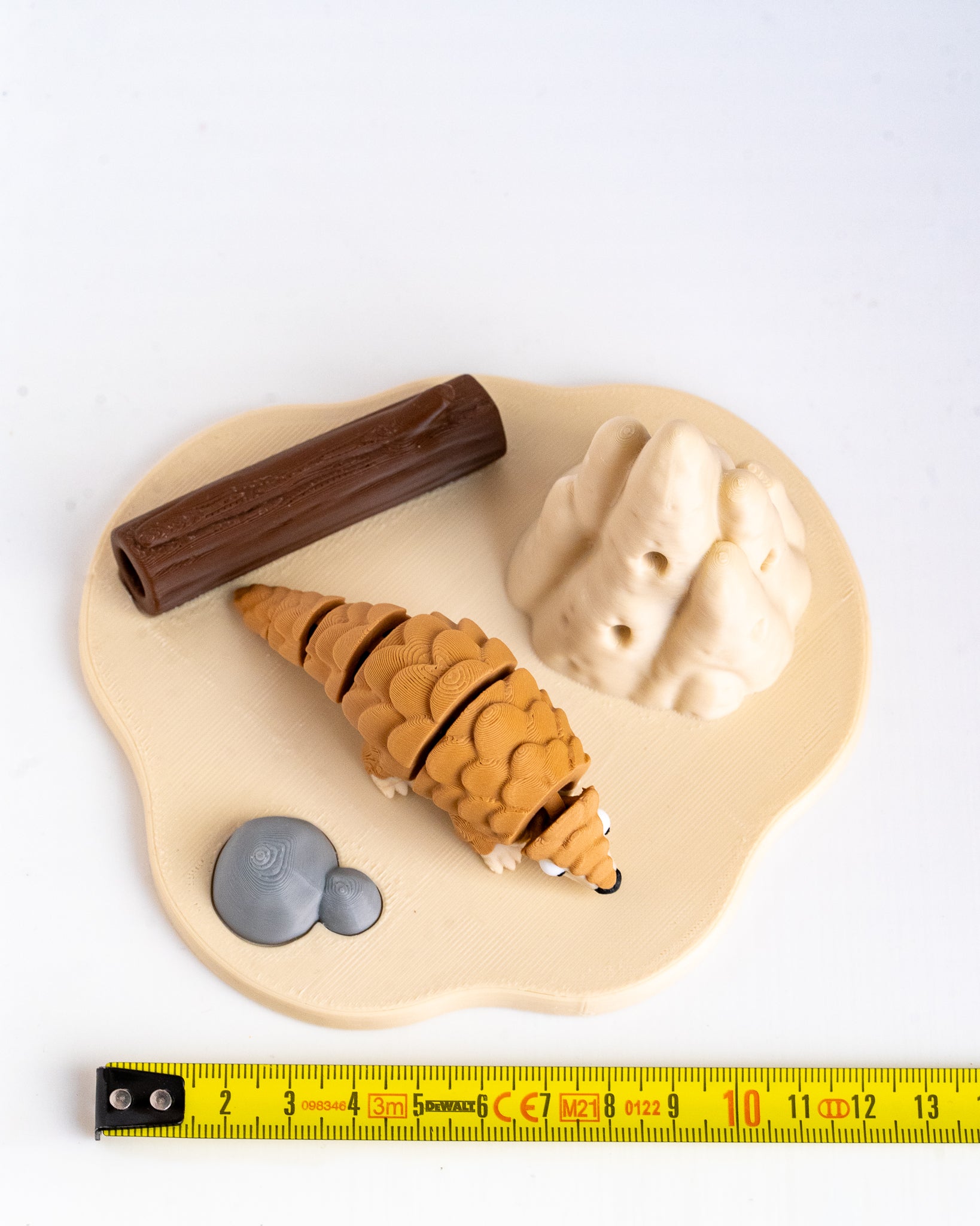 A small animal figurine of a pangolin on a beige base with a brown log, gray rocks, and beige hills, photographed on a white background.