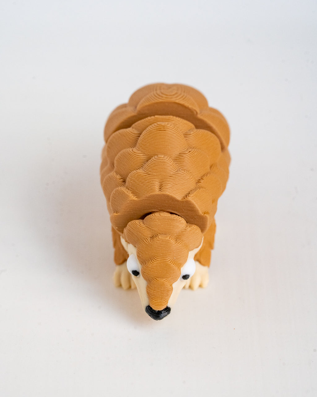 A small 3D-printed articulated pangolin figurine in shades of brown and beige, shown from a top-down view on a plain white background.