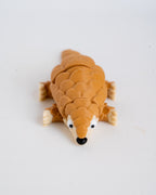 A small pangolin figurine or toy with textured brown scales, cream-colored feet and snout, and a black nose, photographed on a plain light background.