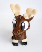 A small moose figurine with a brown body, large cream-colored antlers, and black-and-white legs, photographed against a plain light background.