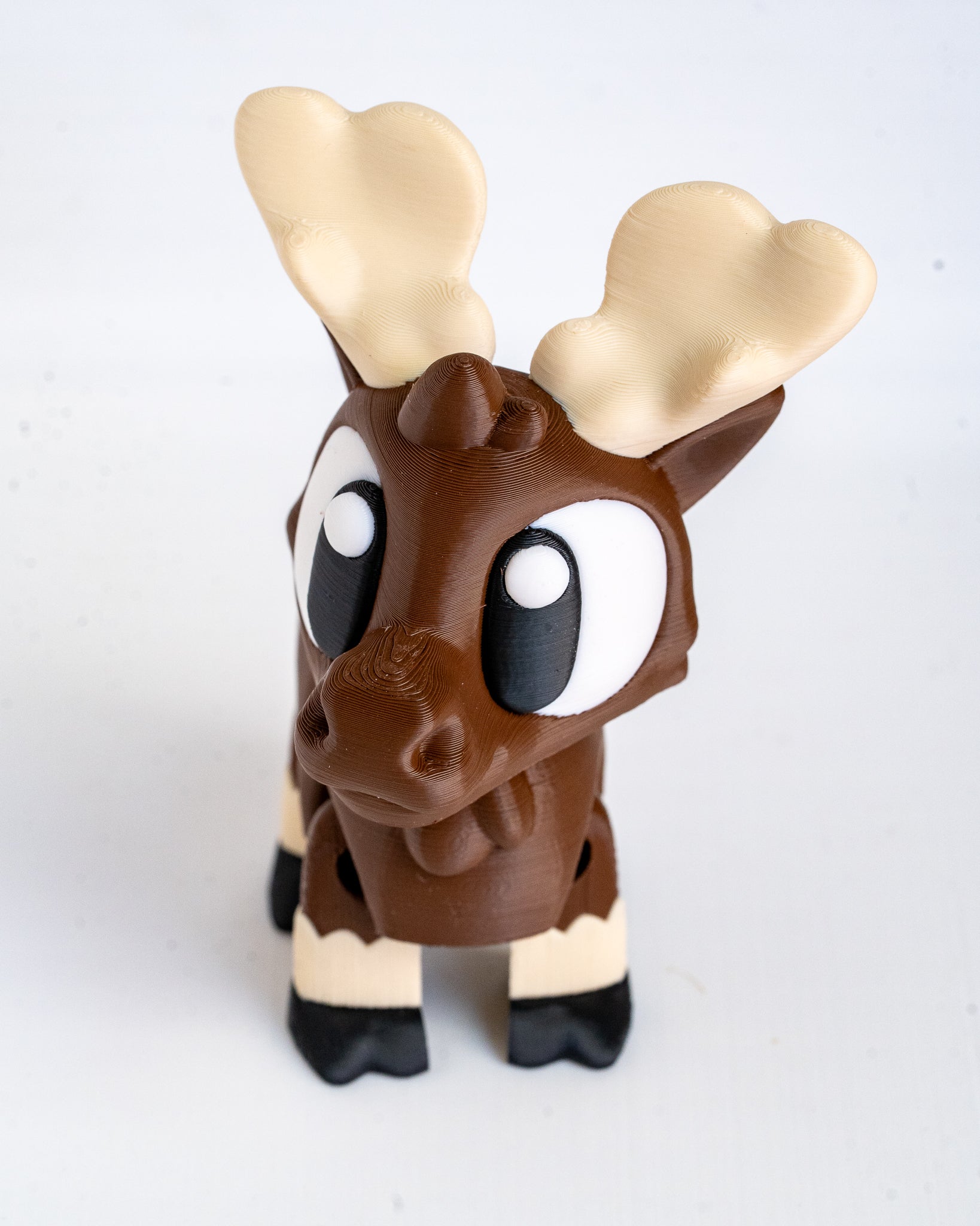 A small moose figurine with a brown body, large cream-colored antlers, and black-and-white legs, photographed against a plain light background.