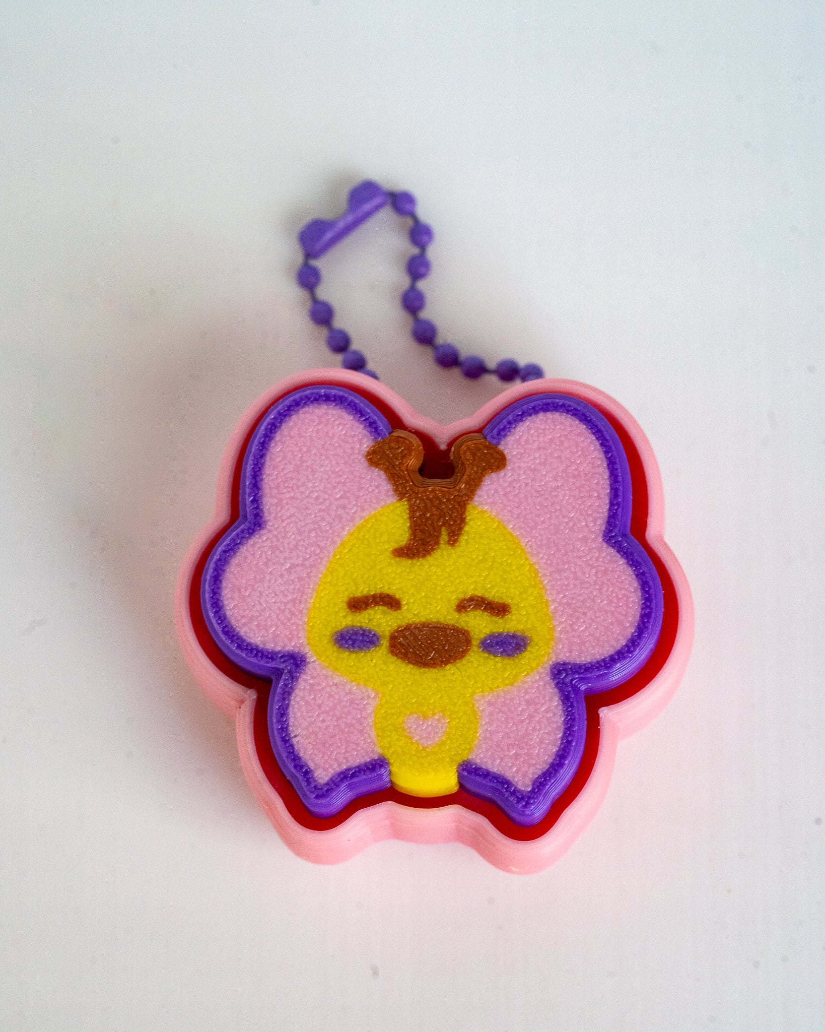 A butterfly-shaped keychain or charm with yellow and pink colors, attached to a purple bead chain on a plain white background.