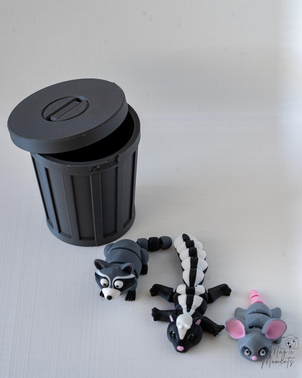 Black trash bin with lid and animal figurines on a light gray surface