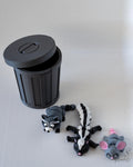 Black trash bin with lid and animal figurines on a light gray surface