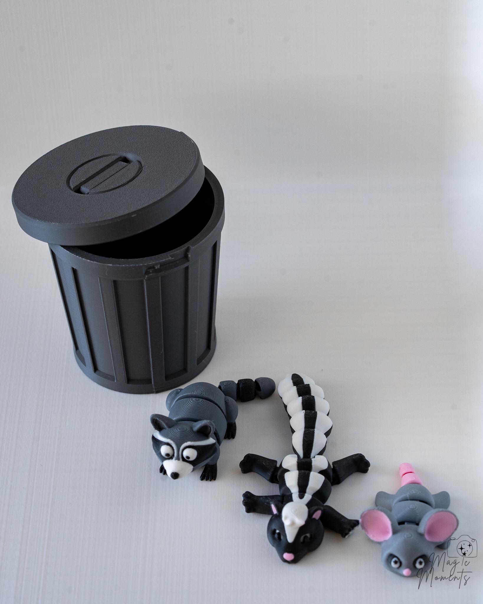 Black trash bin with lid and animal figurines on a light gray surface