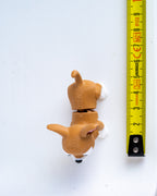 A small dog figurine next to a yellow measuring tape for a scale.