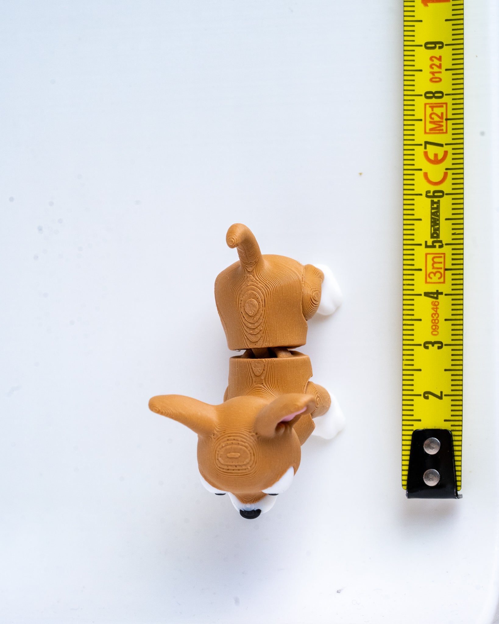 A small dog figurine next to a yellow measuring tape for a scale.